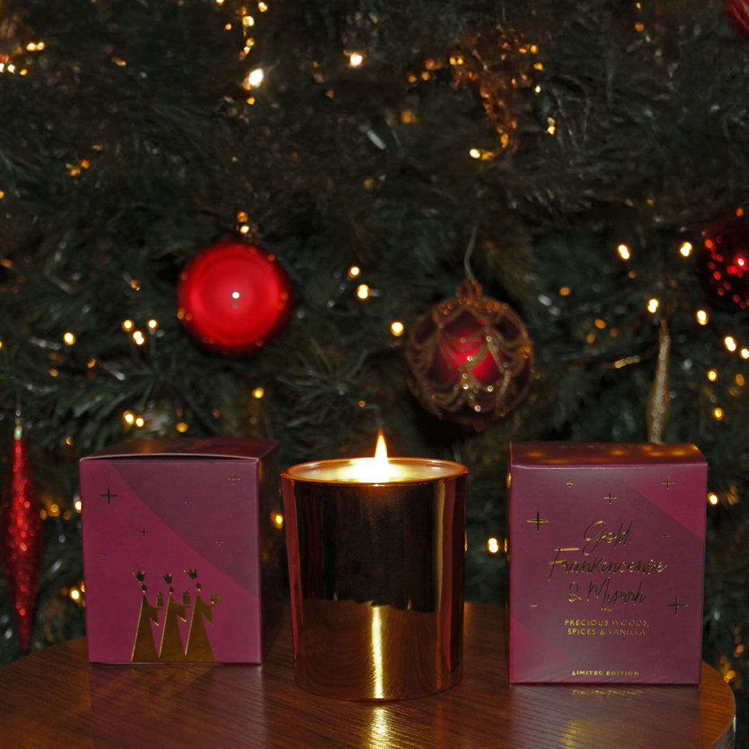 gold candle in jar and gift box in front of Christmas tree